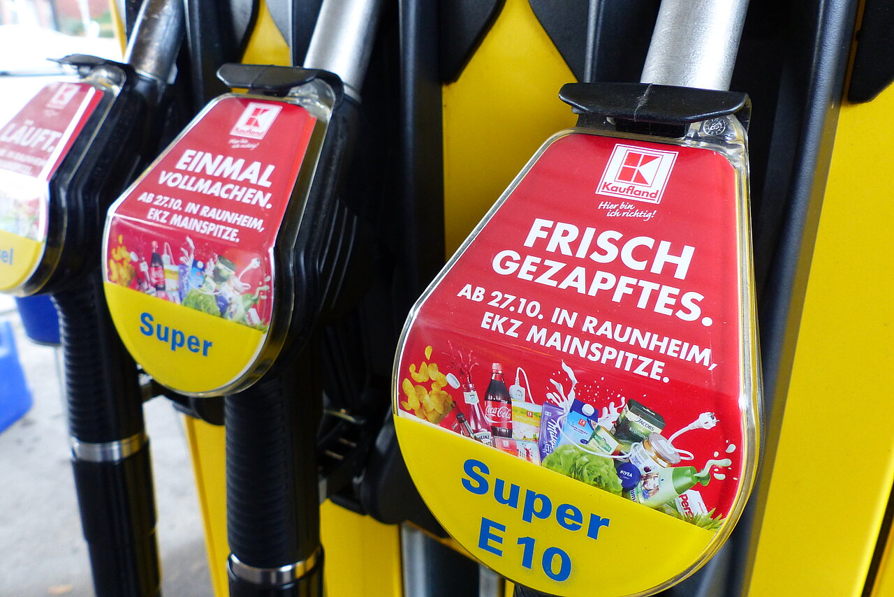 Zapfpistolenwerbung von Kaufland mit rotem Motiv auf Super- und Super-E10-Zapfsäulen an einer Tankstelle
