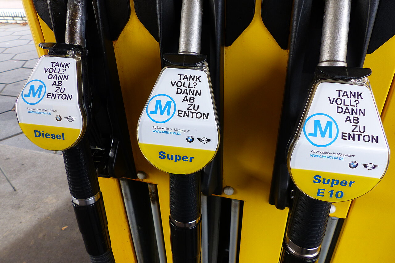 Drei Zapfpistolen mit einheitlicher Ambient-Media-Werbung an einer gelben Tanksäule, beschriftet mit Diesel, Super und Super E10