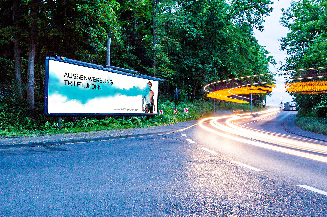 Megastar Plakatwand an einer belebten Straße mit dem Slogan 'AUSSENWERBUNG TRIFFT. JEDEN.' in einer grünen Umgebung. Perfekte Platzierung für auffällige Werbung.