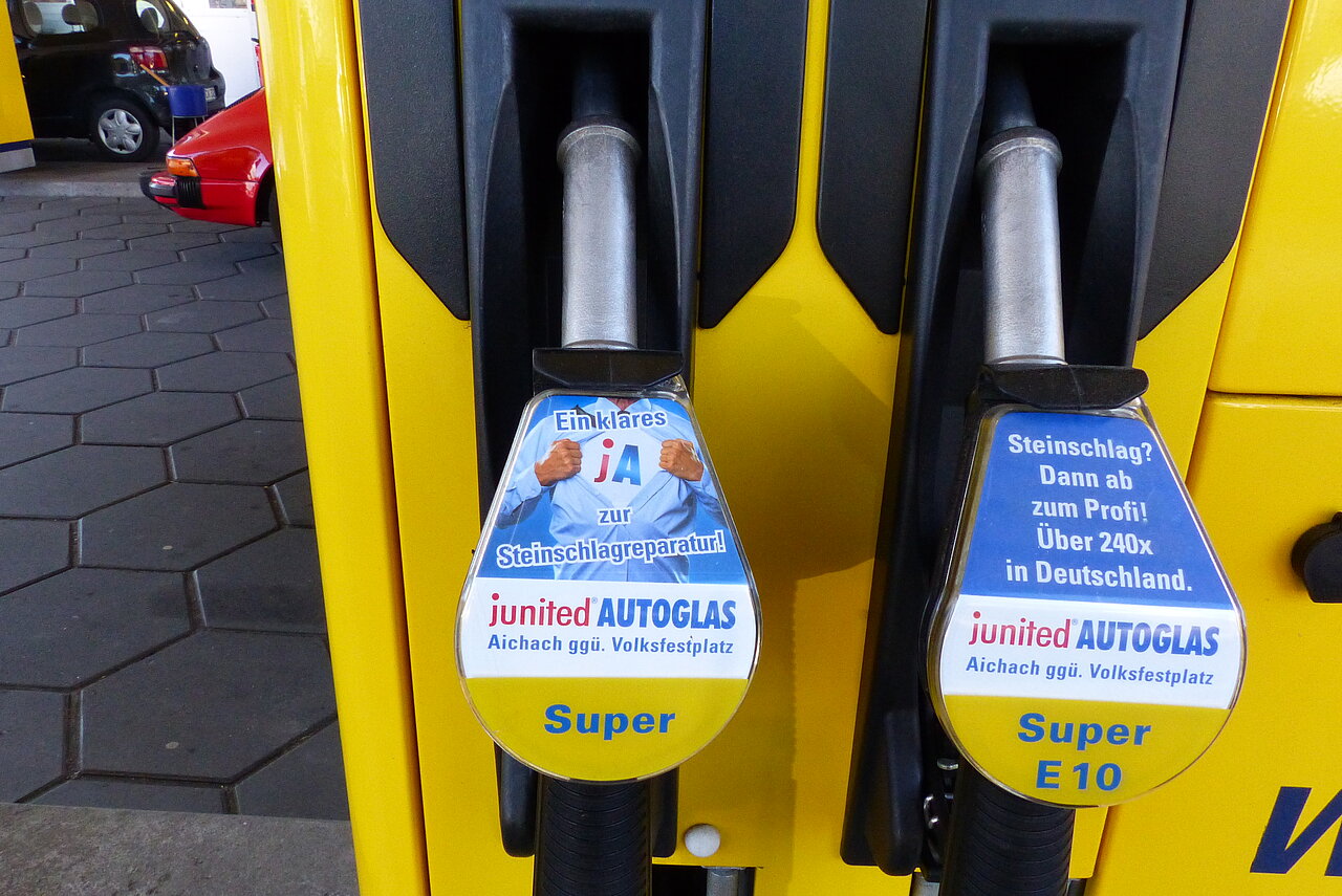 Zapfpistolenwerbung von Junited Autoglas an zwei gelb-schwarzen Tanksäulen für Super und Super E10