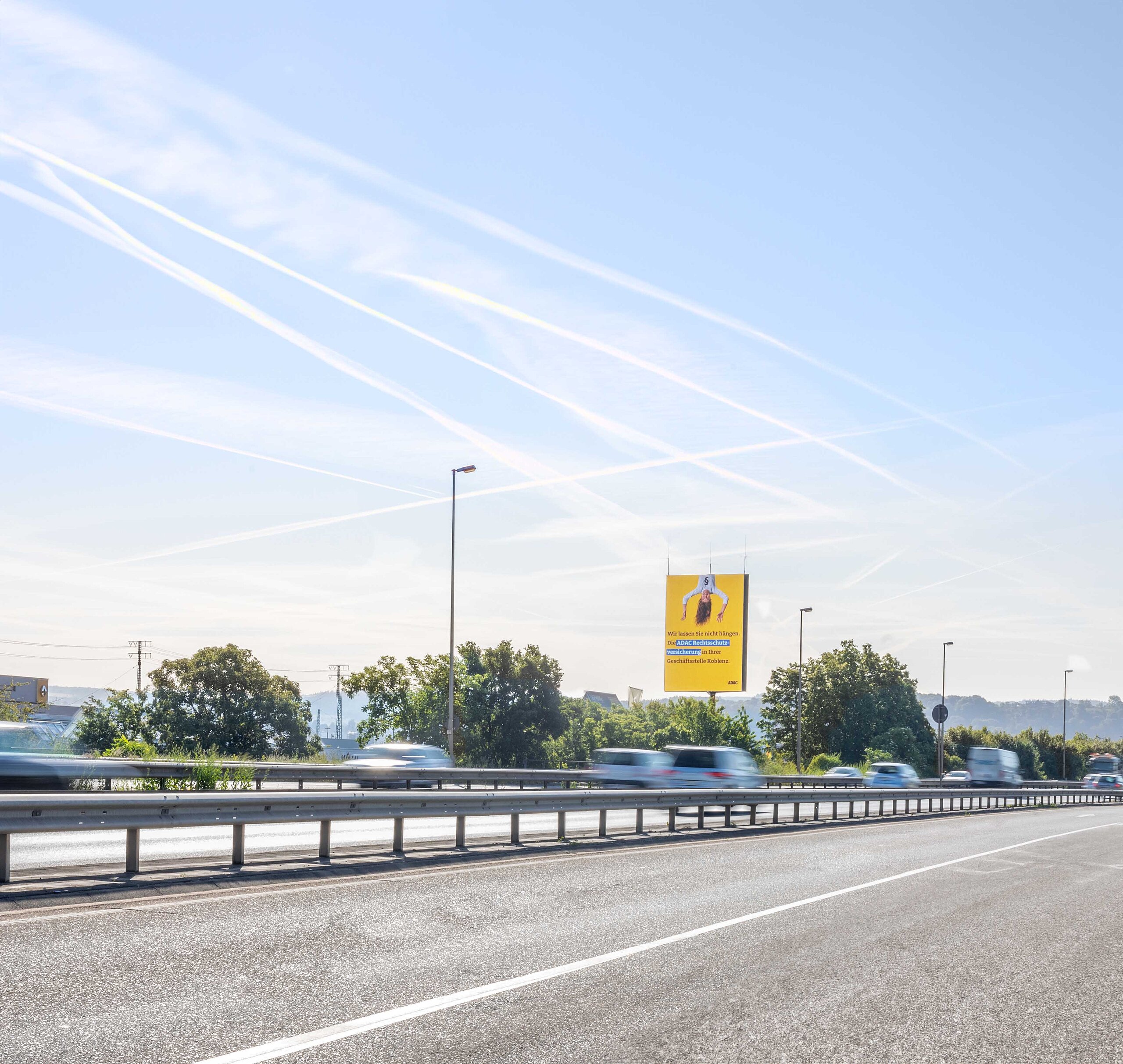Digitaler Tower mit gelber Werbegrafik an einer viel befahrenen Straße, umgeben von vorbeifahrenden Autos und freier Himmel im Hintergrund.