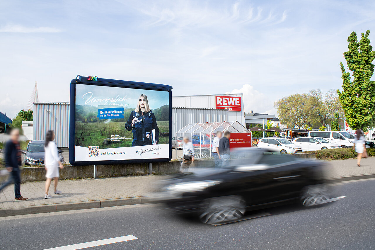 Großplakat an einer Straße neben einem Supermarkt mit einem Recruiting-Motiv einer jungen Person in Uniform, Passanten und vorbeifahrende Autos – buchbar über Plakat-verkauft.de.