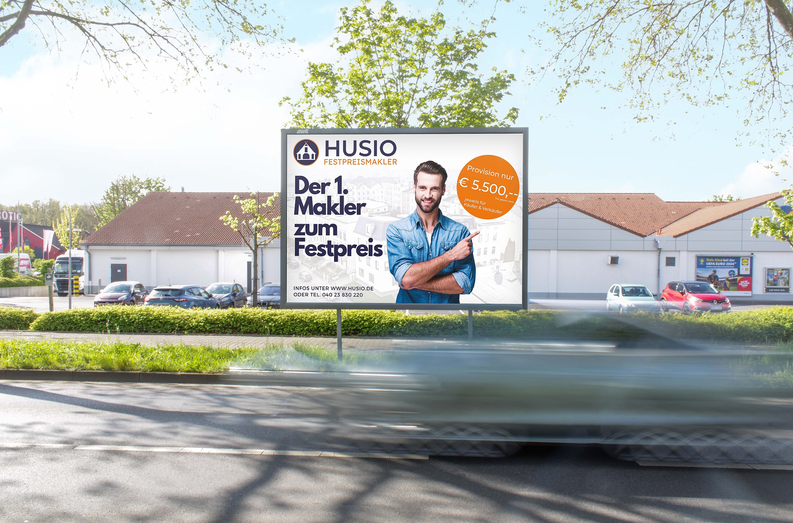 Plakat mit Aufschrift „Der 1. Makler zum Festpreis“ an befahrener Straße vor Gebäuden