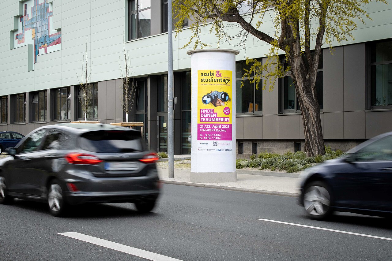 Werbesäule mit buntem Eventplakat für eine Messe, perfekt positioniert an einer viel befahrenen Straße. Deine Werbung auf bis zu 3 Plakaten, rundum sichtbar.