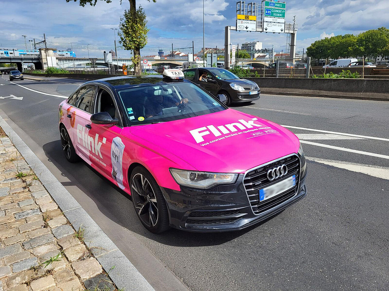 Flink Taxiwerbung auf einem Audi, der in der Stadt fährt. Auffällige pinke Werbung für schnelle Lebensmittel-Lieferung, die für maximale Sichtbarkeit sorgt.