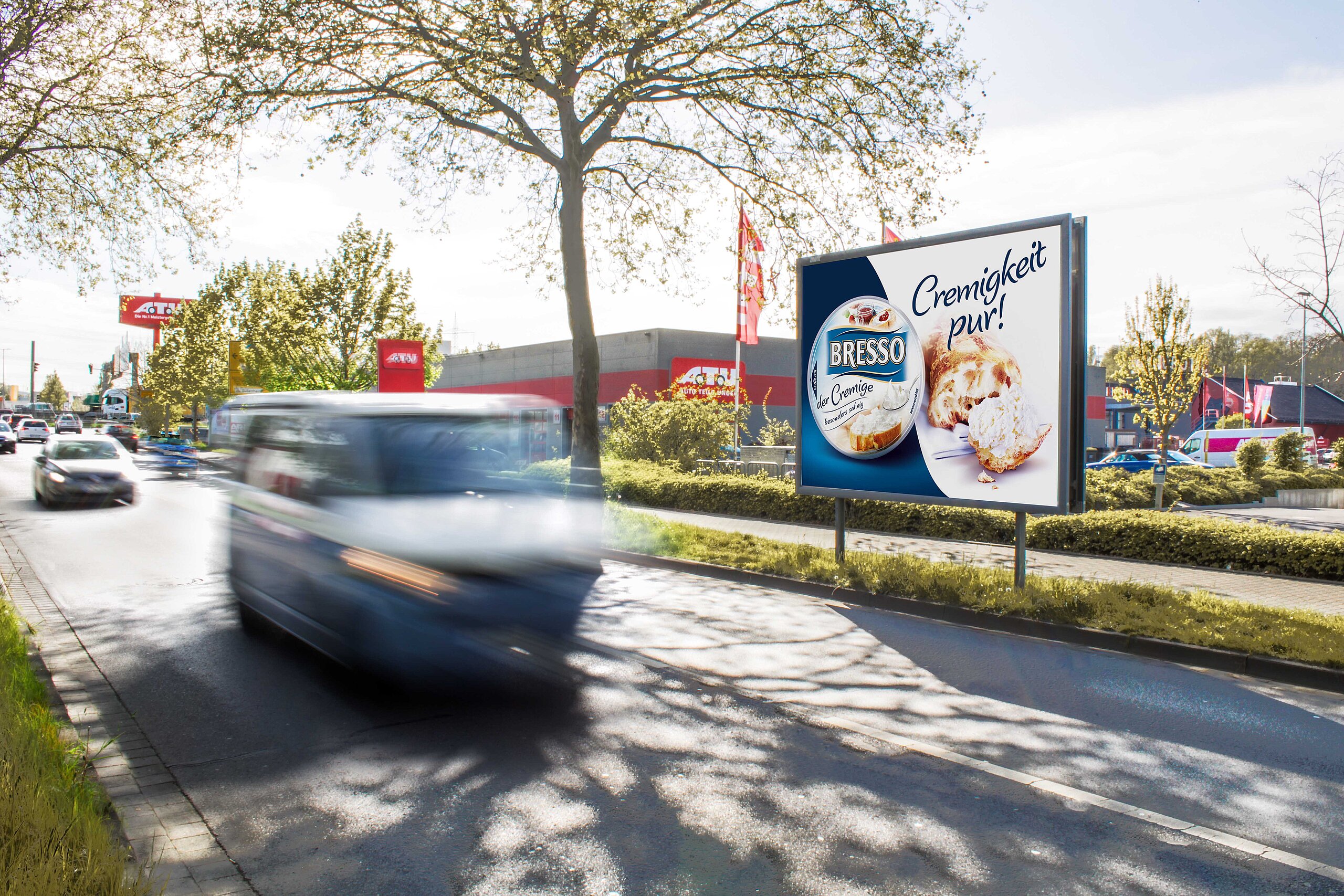 Werbeplakat für Bresso mit dem Slogan 'Cremigkeit pur!' und einem Bild von Bresso und frischem Brötchen. Das Plakat ist gut sichtbar entlang einer belebten Straße.