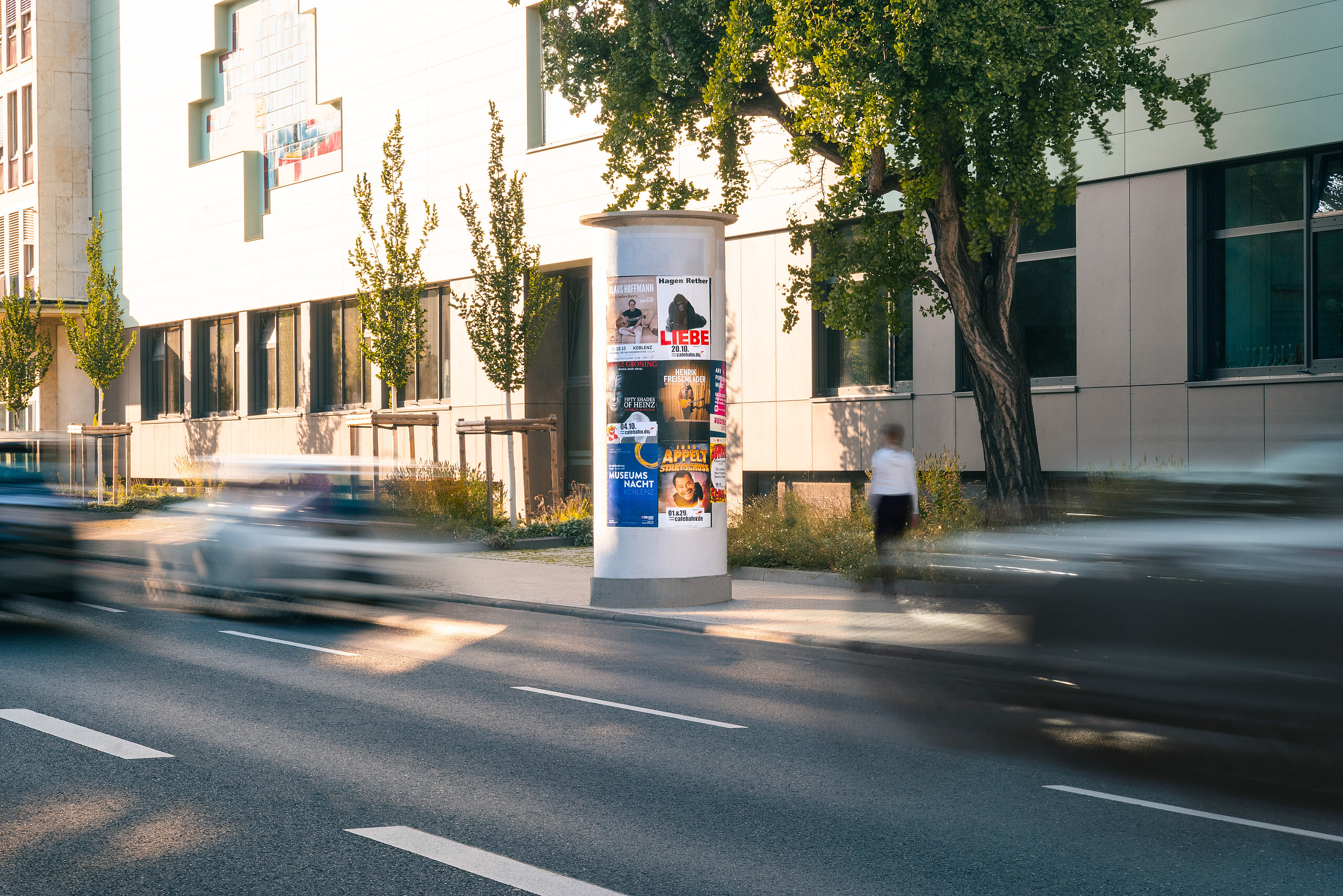 Plakatsäule an einer städtischen Straße bei Tageslicht mit mehreren Veranstaltungsplakaten