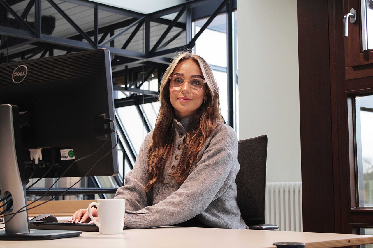 Mitarbeiterin sitzt an ihrem Arbeitsplatz im lichtdurchfluteten Büro von Plakat-verkauft.de
