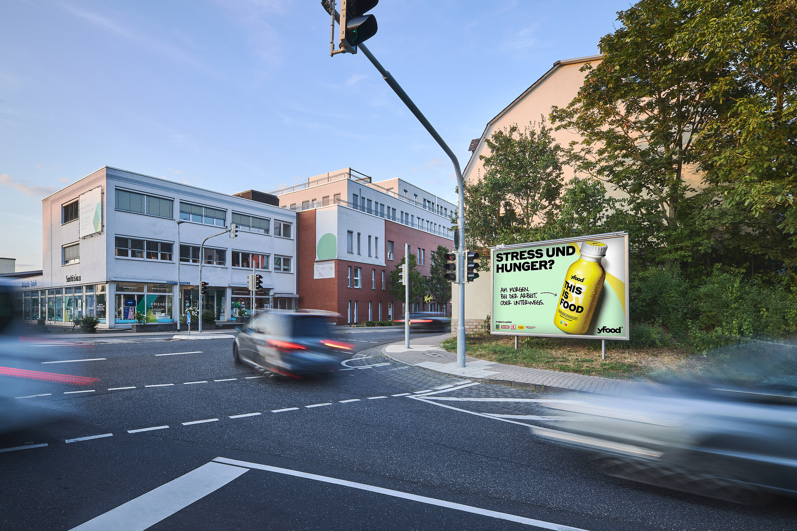 Werbeplakat für yfood mit dem Slogan 'Stress und Hunger?' und einem Bild der Produktflasche. Das Plakat ist an einer belebten Straßenecke gut sichtbar für Autofahrer und Passanten.