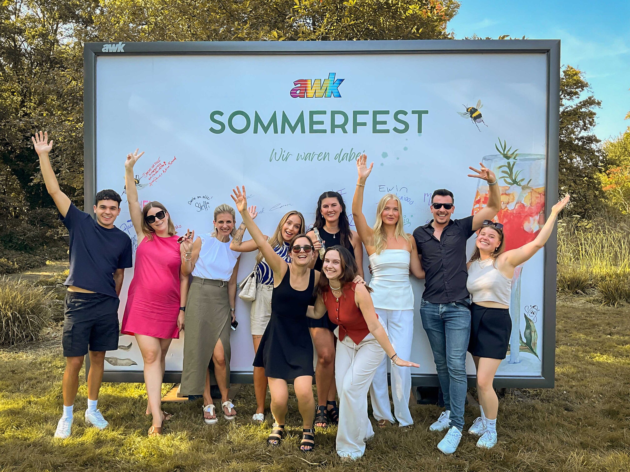 Mitarbeitende von Plakat-verkauft.de feiern gemeinsam beim Sommerfest und posieren lachend vor einer Großfläche