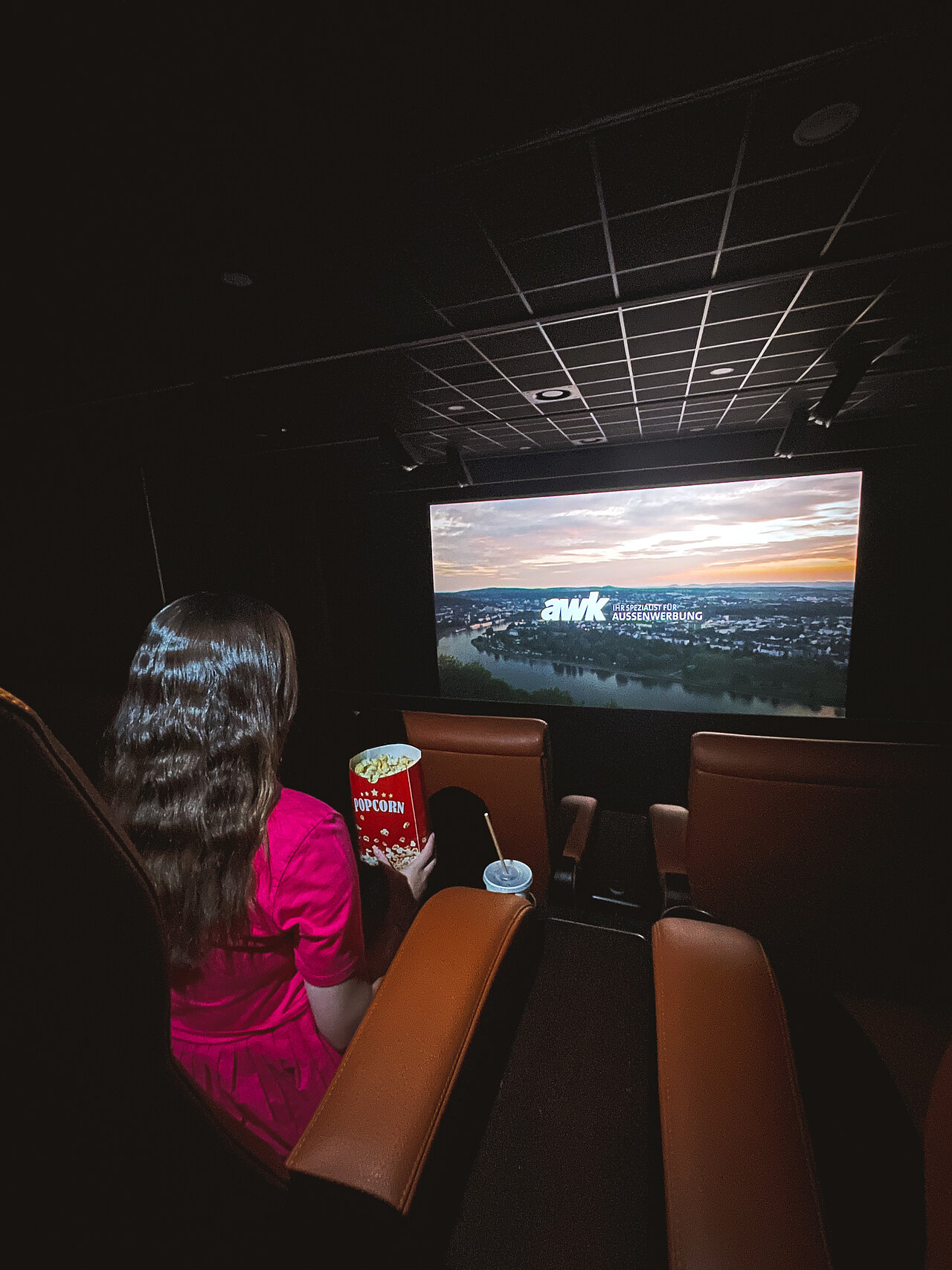 Kinowerbung in einem Kino mit einer Frau, die Popcorn isst und die Leinwand betrachtet. Der Kinospot wird groß im Kinosaal präsentiert.