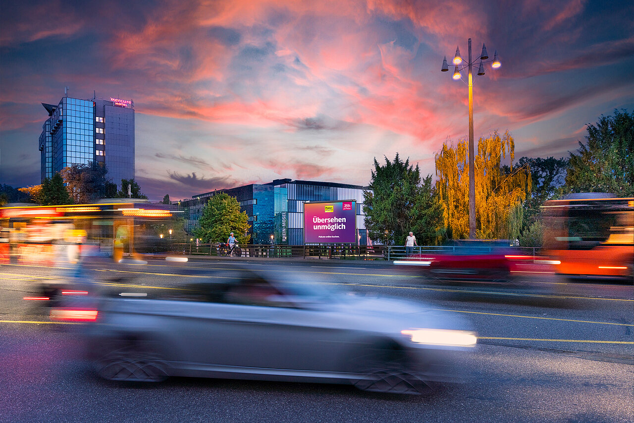 Werbeplakat mit dem Slogan 'Übersehen unmöglich' an einer belebten Brücke. Es ist gut sichtbar für vorbeifahrende Autos und Fußgänger in einer stark frequentierten Gegend.