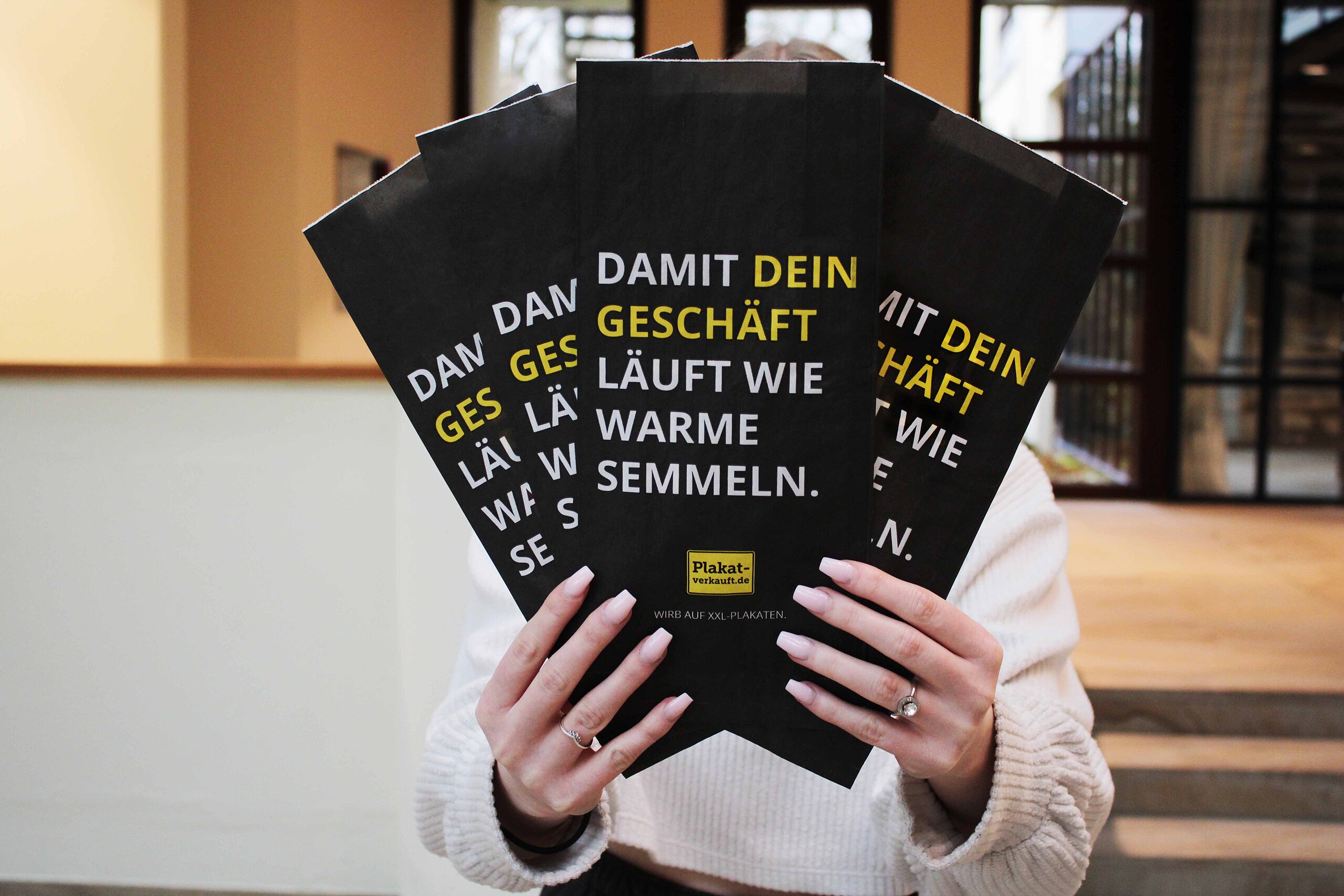 Person hält mehrere schwarze Brötchentüten mit Werbeslogan „Damit dein Geschäft läuft wie warme Semmeln“ – Beispiel für Ambient Media Werbung auf Brötchentüten