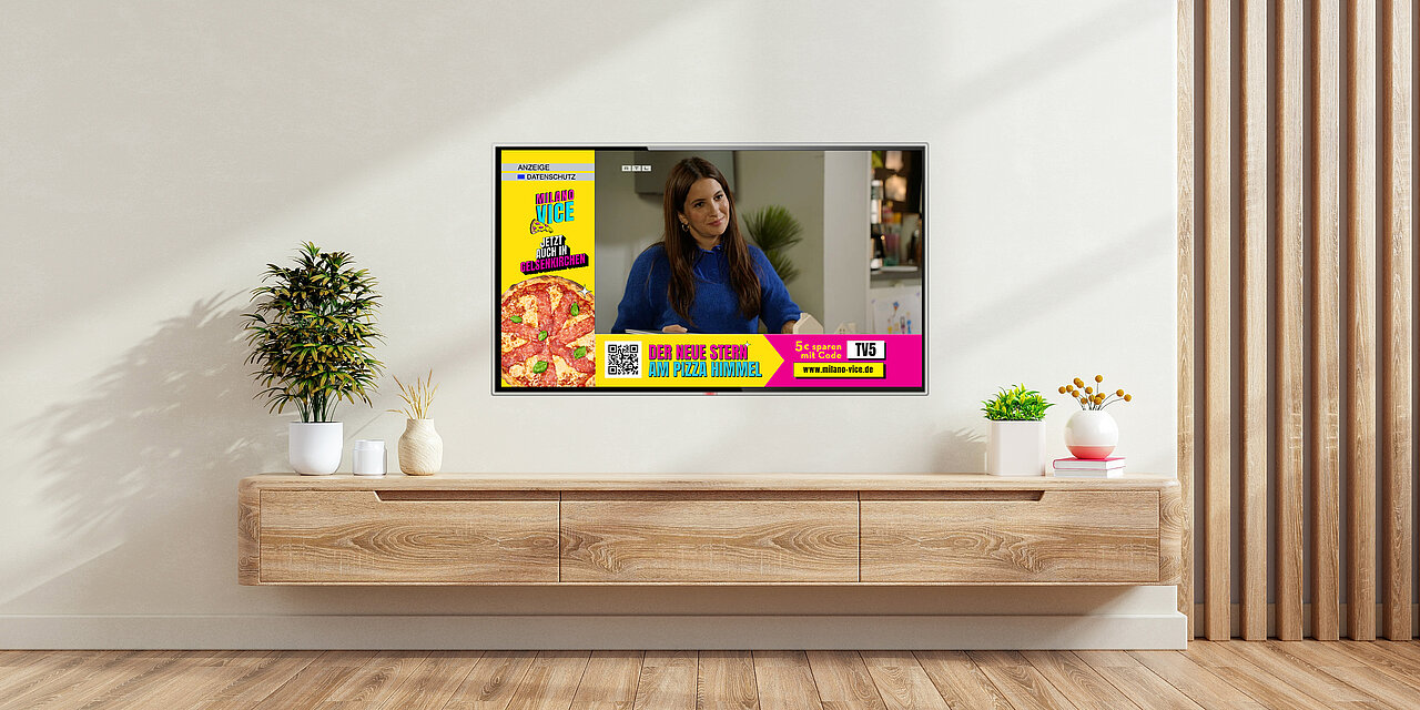 Modernes Wohnzimmer mit Wandfernseher, auf dem eine Addressable-TV-Werbung für Pizza erscheint, kombiniert mit laufendem TV-Programm.