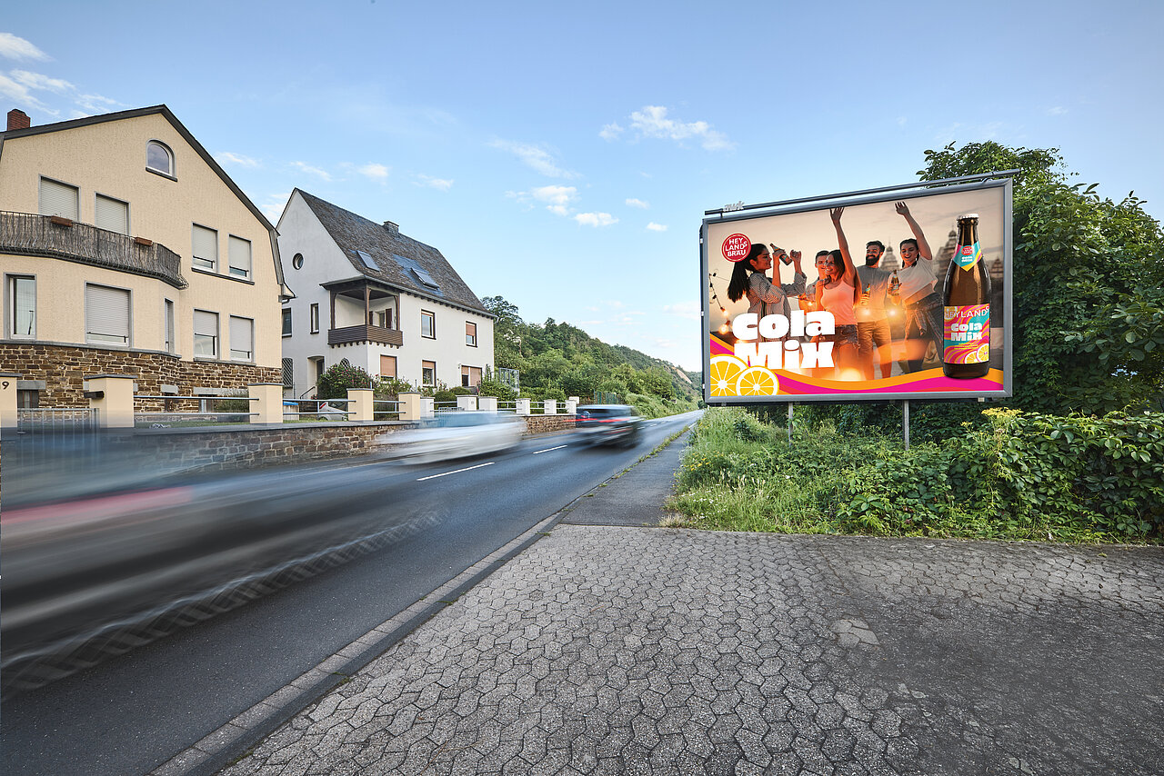 Großes Werbeplakat an einer Durchfahrtsstraße mit fröhlicher Cola-Mix-Anzeige, Autos fahren schnell vorbei – buchbar über Plakat-verkauft.de.